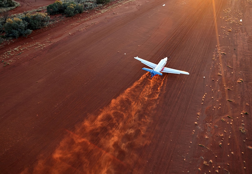 A Royal Flying Doctor Service plane landing on a red sand airstrip.