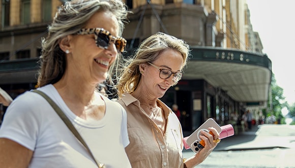 two women wearing sunglasses walk down a street