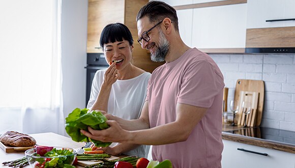A man and woman stand in their kitchen preparing fresh produce