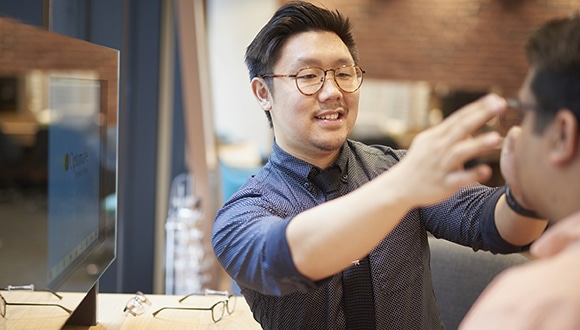 A male optometrist places glasses onto a client's face