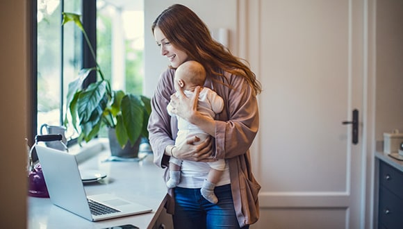 New mother holding her baby while on her lapop