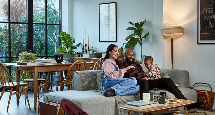 A couple sitting on the couch smiling with their young child.