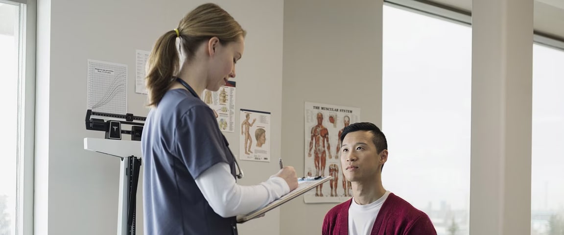 A female doctor holding a clipboard assessing a male patient sitting down.