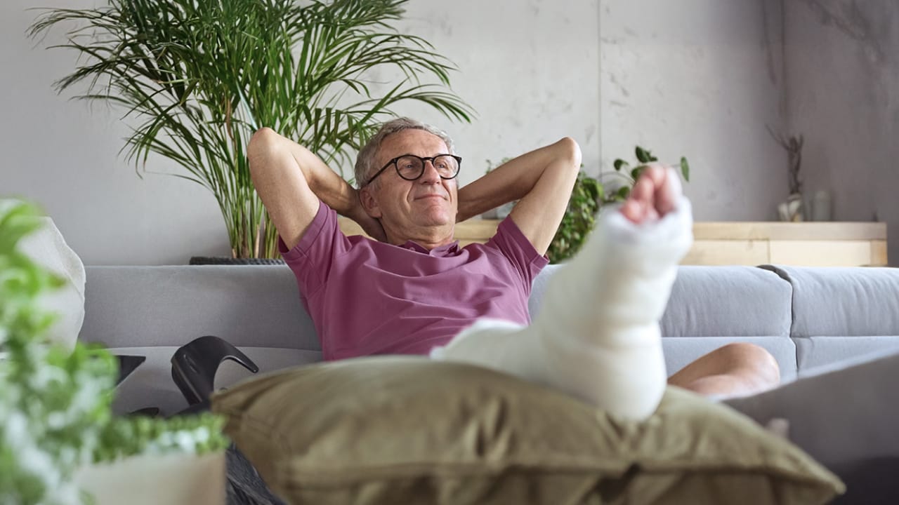 A man sitting on the lounge with a broken leg in a cast.