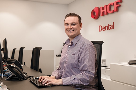 A specialist sitting at his desk in front of a computer in front of HCF dental insurance sign.