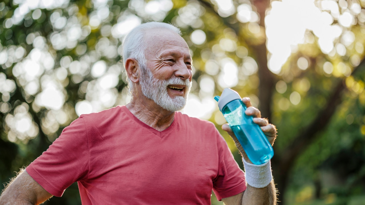 Man smiling while drinking from a bottle of water while outdoors.
