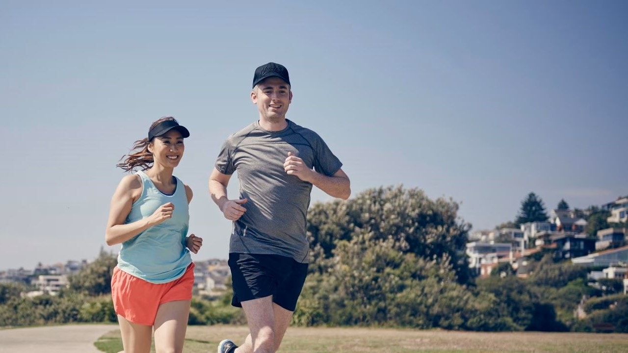Man and woman outdoors running together in the sunshine.