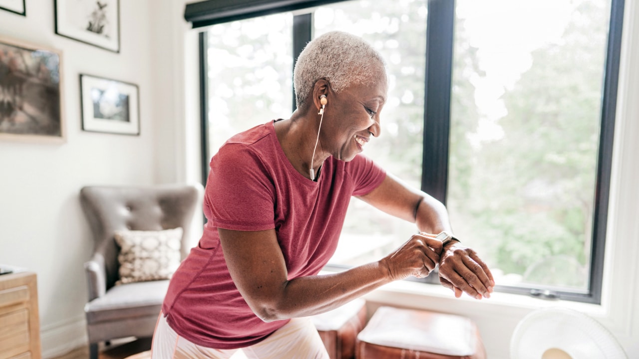 An older woman using her smartwatch while wearing athletics clothing at home.