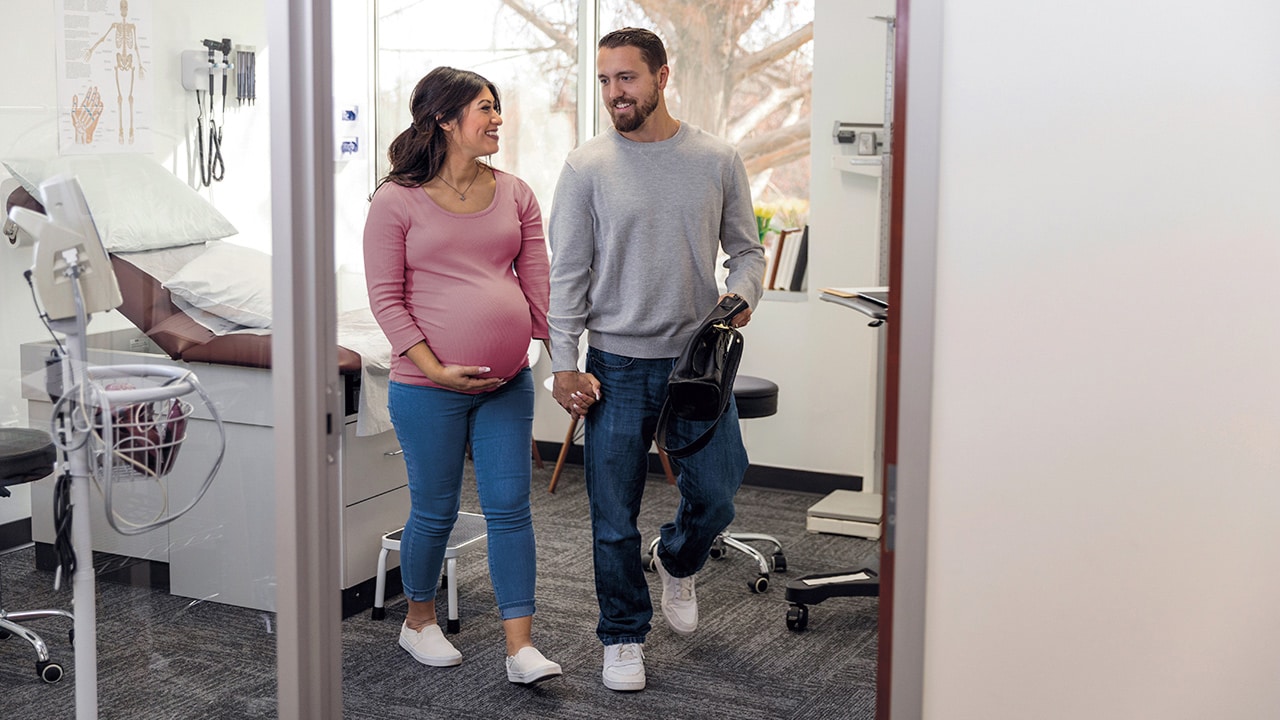 A pregnant woman walks out of a hospital room with her male partner.