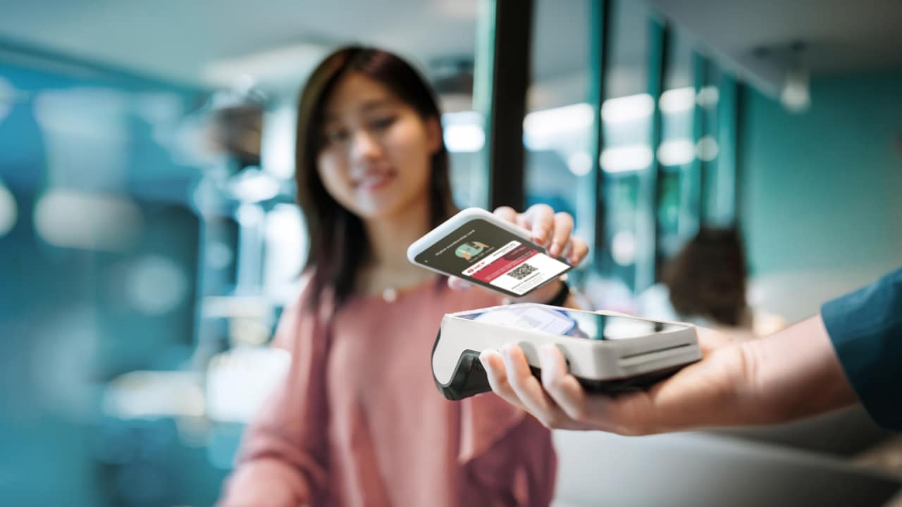 A young woman using her smartphone to tap her digital card at a terminal.