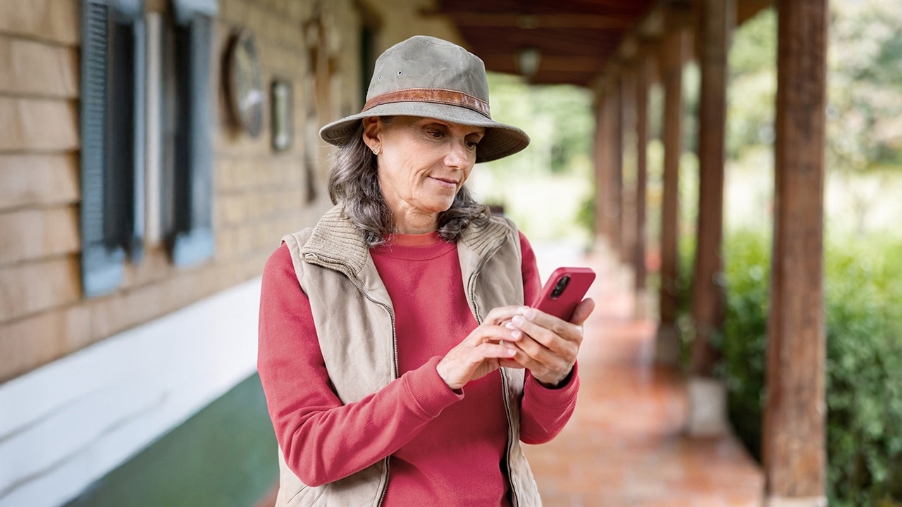 A woman wearing a hat stands outdoors and looks at her phone.