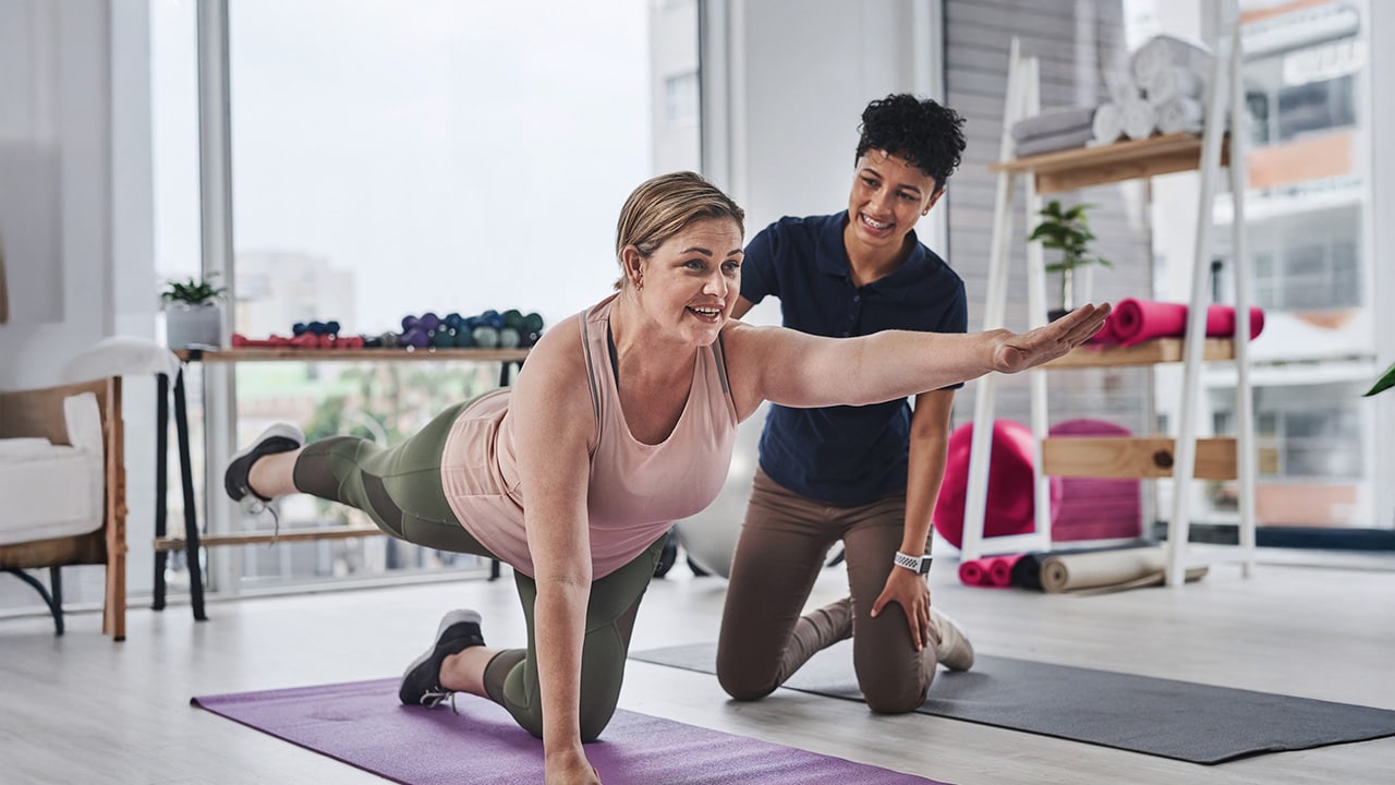 Woman stretches on mat with help on physical therapist.