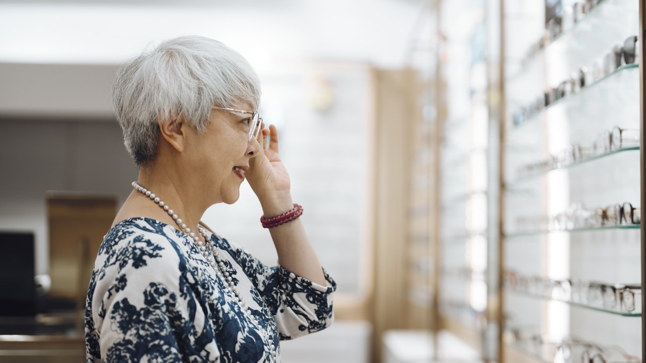 A woman smiling trying on a pair of glasses in front of a mirror.
