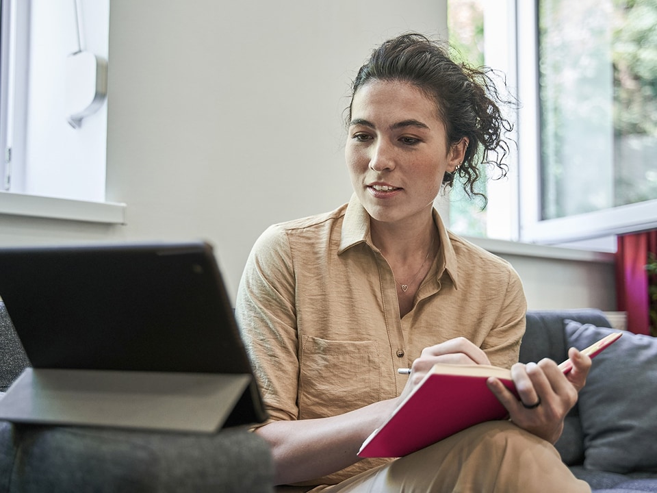 A woman sitting on the lounge with her notepad and laptop.